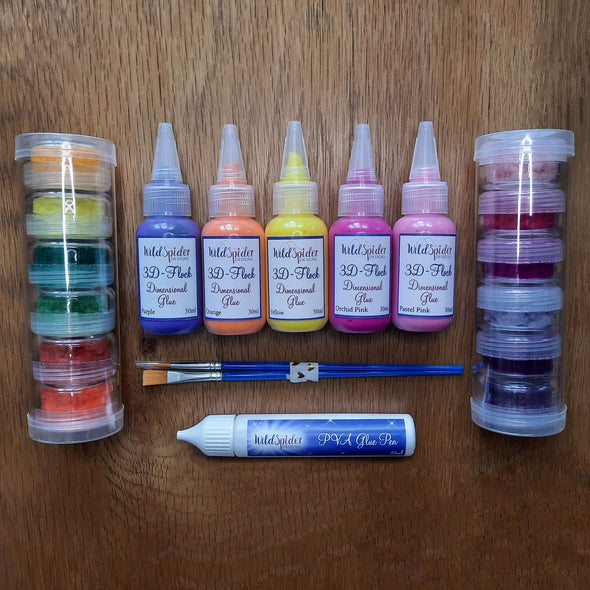 3D-Flock Dimensional Glue Super Kit, 5 bottles of 3D glue in Yellow, Orange, Pastel Pink, Orchid Pink and Purple, 2 brushes, 2 tubes of 10ml pot flocks and a glue pen placed down on a table