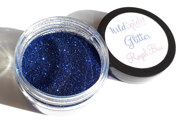 Royal Blue glitter in an open jar next to it's lid. Sparkles of glitter are shining in the sun.